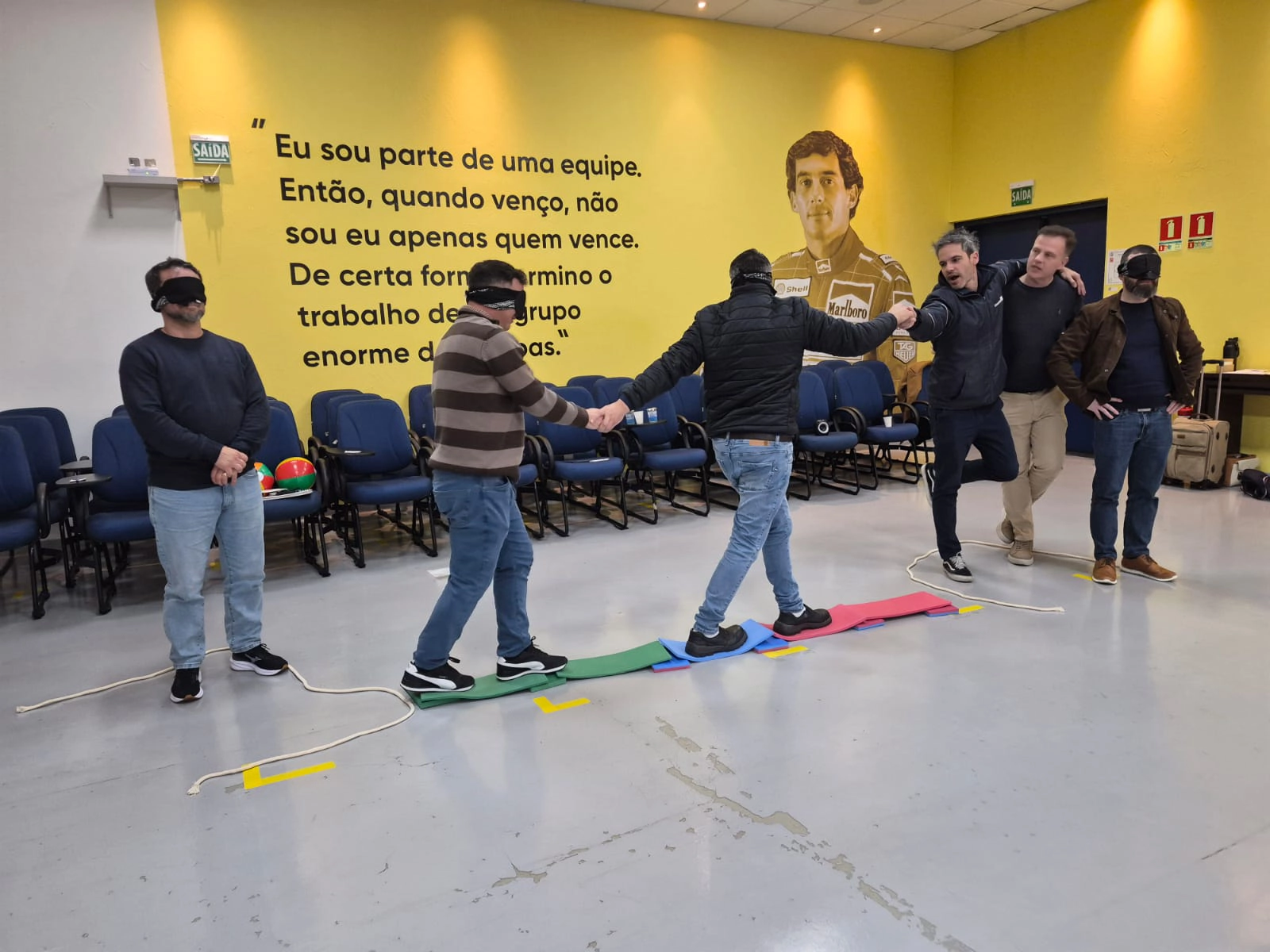 Participantes vendados, de quatro apoios, montando a ponte de tábuas no desafio As Ilhas