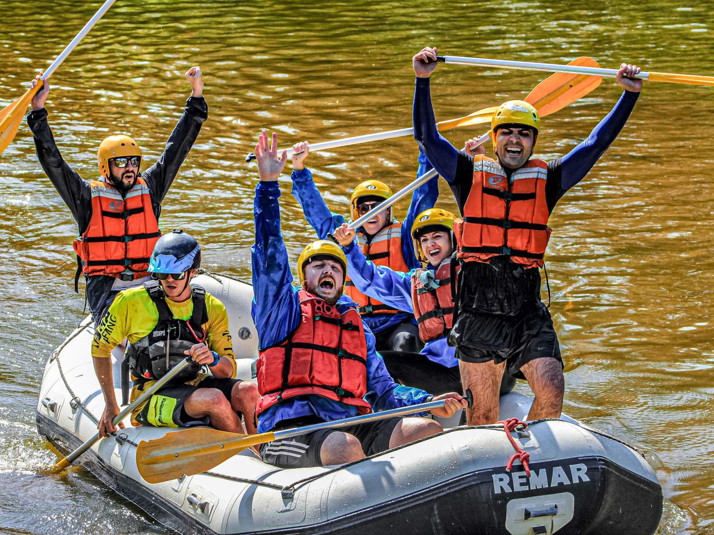 Equipe comemorando com os remos para cima durante um desafio de rafting da Outbox