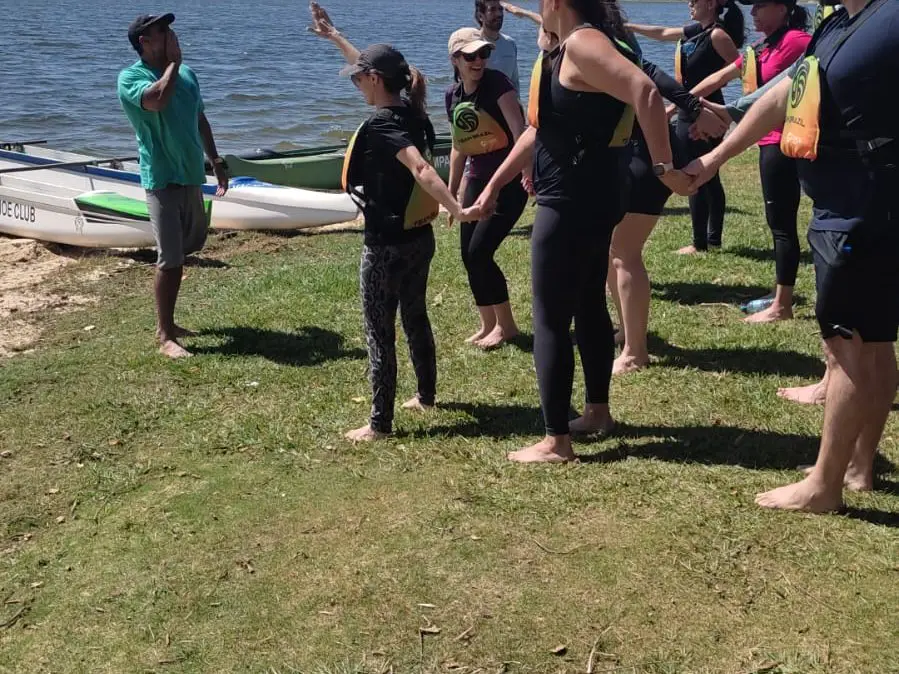 Líderes em dinâmica de aquecimento no gramado, à beira da represa, antes da canoa
